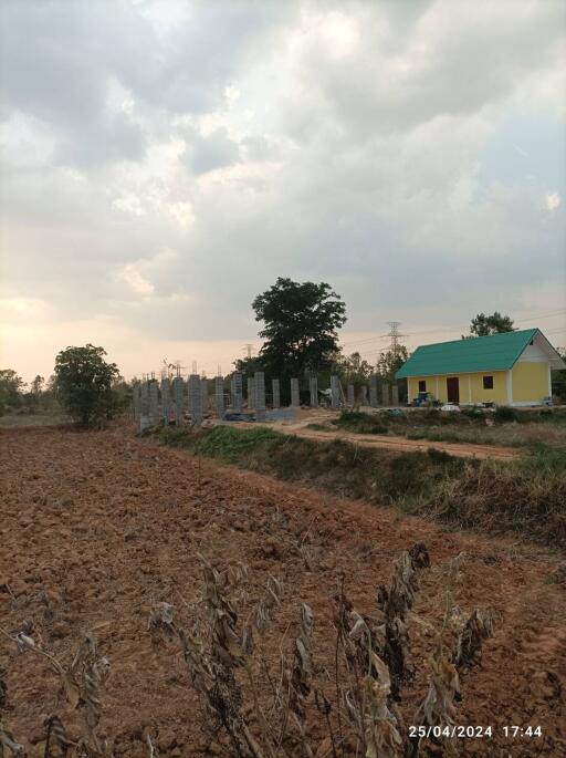 Wide view of a plowed field, adjacent to a partially built structure and a small house.