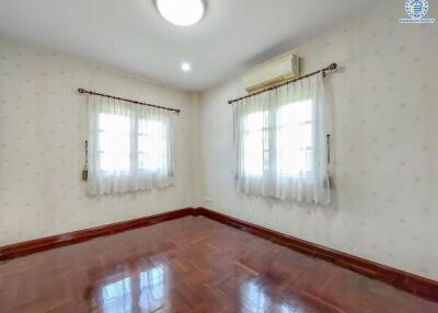 Empty bedroom with wooden flooring and two windows with white curtains