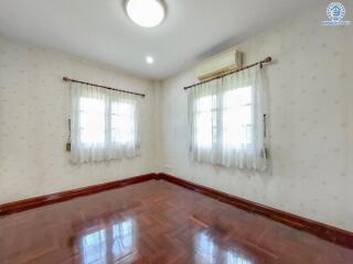 Empty bedroom with wooden flooring and two windows with white curtains