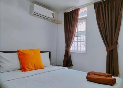 A bedroom with a neatly made bed, a window with brown curtains, and an air conditioning unit.