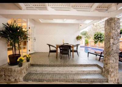 Covered patio area with dining table and chairs near a pool