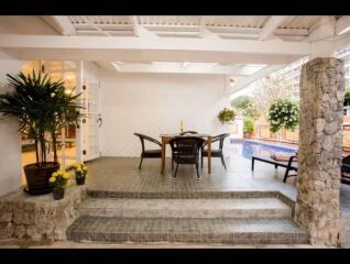 Covered patio area with dining table and chairs near a pool