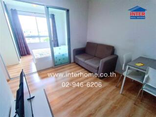 Modern living area with wooden floor, sofa, TV, dining table, and bedroom visible through sliding glass doors