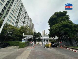 Entrance of a residential building complex with trees and parked cars