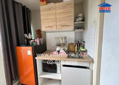 Compact kitchen area with orange refrigerator, wooden cabinets, microwave, and various kitchen appliances