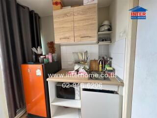 Compact kitchen area with orange refrigerator, wooden cabinets, microwave, and various kitchen appliances