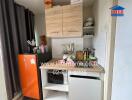 Compact kitchen area with orange refrigerator, wooden cabinets, microwave, and various kitchen appliances