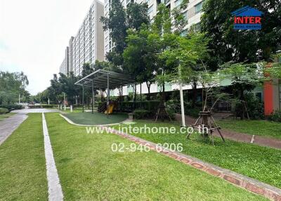 Outdoor garden area with green lawn and trees alongside a tall apartment building