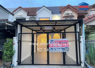 Front view of a house with a carport and a sign for sale by a real estate agency