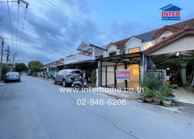 Street view of residential buildings with cars parked in front, featuring a real estate sign.