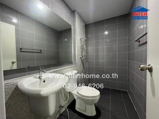 Modern bathroom with gray tiled walls, a shower, toilet, and sink