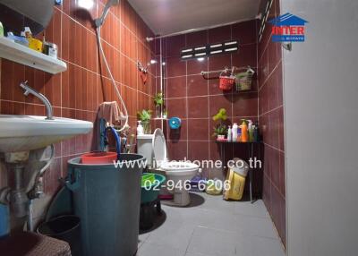 Bathroom with brown tiles, sink, toilet, and various cleaning supplies