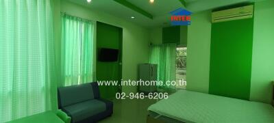 Bedroom with green decor including double bed, sofa, curtains, air conditioner, and television.