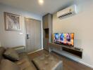 Modern living room with gray sofa, wall-mounted TV, and air conditioning unit