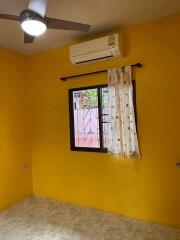 Bedroom with yellow walls, window with curtain, ceiling fan, and air conditioner