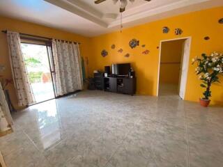 Spacious living room with decorative yellow wall, tiled floor, TV stand, ceiling fan, and sliding glass door to patio