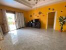 Spacious living room with decorative yellow wall, tiled floor, TV stand, ceiling fan, and sliding glass door to patio