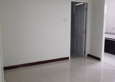 Photo of a room with white walls and tiles, showing a door leading to a kitchen area