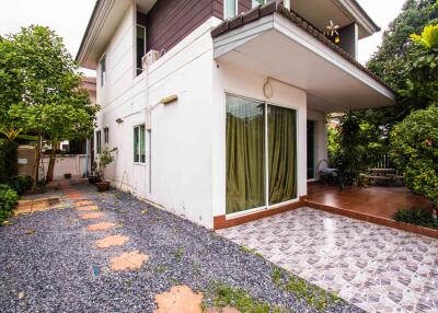 View of the exterior side of a two-story house with tile and gravel pathways, surrounded by greenery