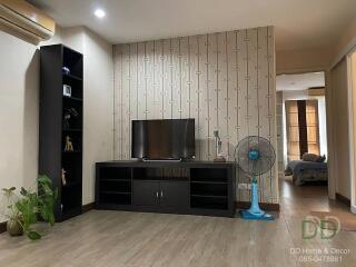 Living room with a TV stand, shelves, and a fan, showing an adjoining bedroom