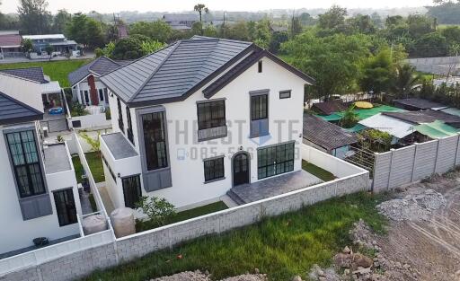 Aerial view of a modern two-story house with surrounding greenery and neighboring properties