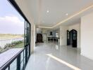 View of a modern, open-concept living room with large windows and a view of the kitchen area