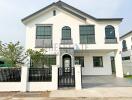 White two-story house with black window frames and gated front yard