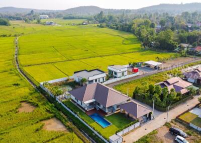 Aerial view of a residential house with a pool and surrounding green fields