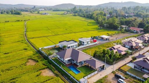 Aerial view of a residential house with a pool and surrounding green fields