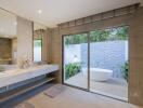 Modern bathroom with double sinks, large mirror, and view of outdoor bath