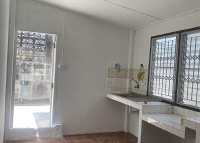 A simple kitchen with tiled flooring, a sink area, and a window with bars.