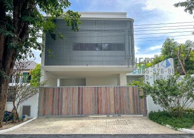 Modern two-story house exterior with gated entrance and trees