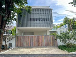 Modern two-story house exterior with gated entrance and trees