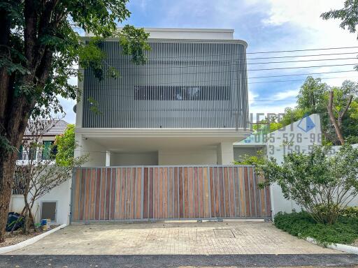 Modern two-story house exterior with gated entrance and trees