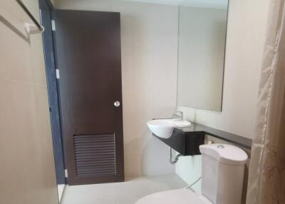 Modern bathroom with a toilet, sink, large mirror, and a door