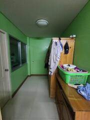 Small narrow bedroom with green walls, wooden furniture, and hanging clothes