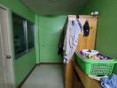 Small narrow bedroom with green walls, wooden furniture, and hanging clothes