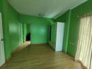 Green-painted bedroom with wooden flooring, wardrobe, and large window