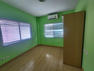 A brightly lit and freshly painted bedroom with light wooden flooring and air conditioning.