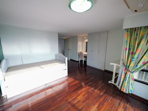 Spacious bedroom with wooden floor, single bed, desk, and ample storage