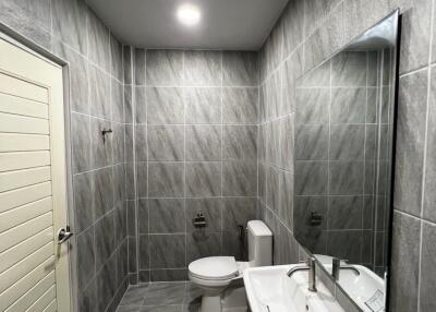 Modern bathroom with grey tiled walls and floor, white toilet and sink.