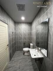 Modern bathroom with grey tiled walls and floor, white toilet and sink.