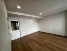 Spacious empty room with wooden flooring and recessed lighting