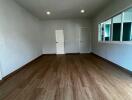 Spacious empty living room with wood flooring and white walls