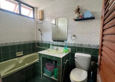 Bathroom with green and white tiles, bathtub, toilet, sink, mirror, and small shelf