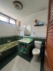 Bathroom with green and white tiles, bathtub, toilet, sink, mirror, and small shelf