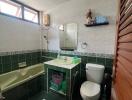 Bathroom with green and white tiles, bathtub, toilet, sink, mirror, and small shelf