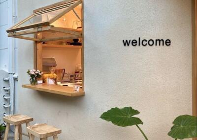 Small outdoor cafe window with wooden stools and welcome sign