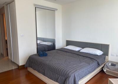 Modern bedroom with wooden flooring, king-sized bed, bedside table, mirror, and door to an adjacent room