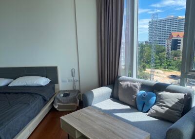 Bright bedroom with bed and sofa, featuring a large window with an urban view